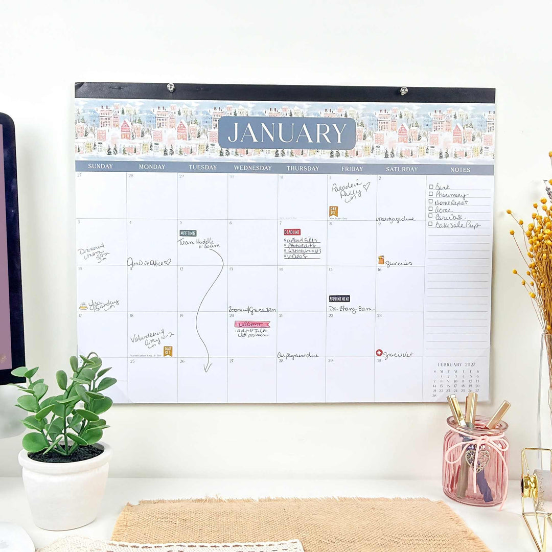 Wall calendar for January on a white wall with a plant and desk items below.