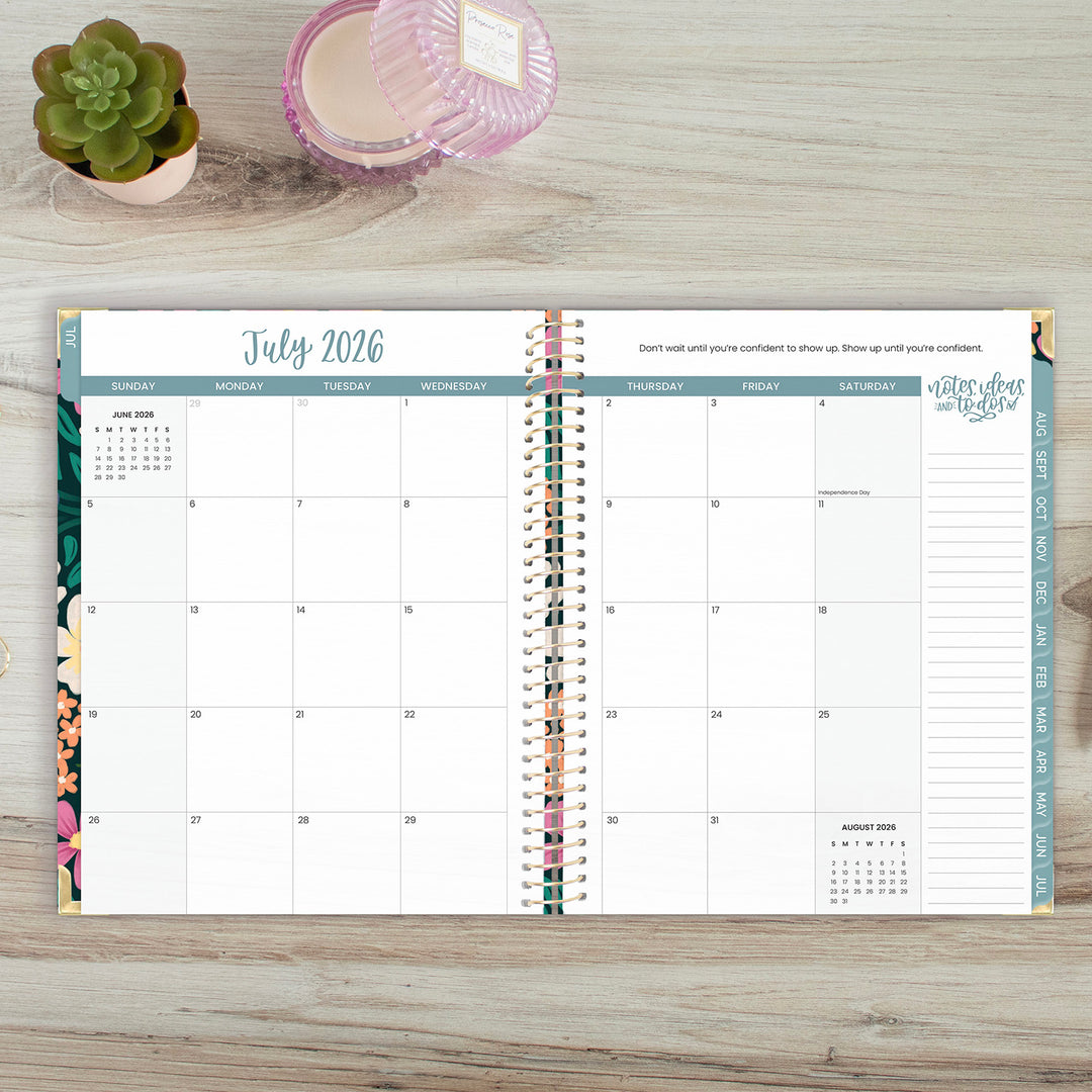 Calendar planner open to July 2026 on a wooden surface with decorative items.