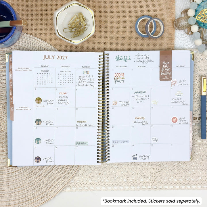 Open Christian planner with spiral binding and dated July 2027 monthly view