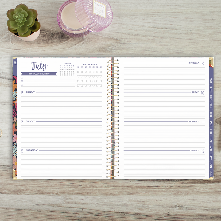 Open planner on a wooden surface with a small plant and pink container.