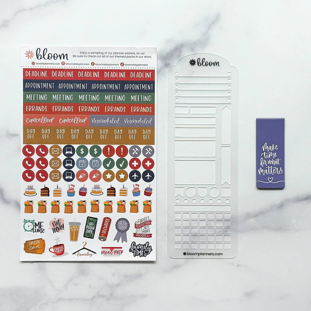 Bloom planner sticker set and accessories displayed on a white marble background, including a sheet of multicolor text and icon stickers, a white planner divider, and a purple sticky note.