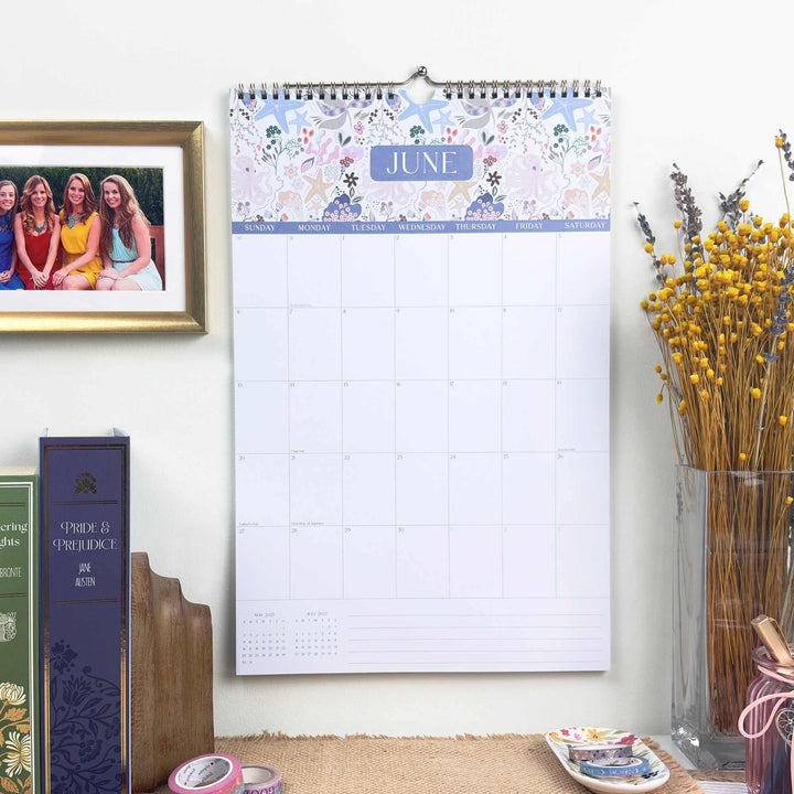 Wall calendar for June with decorative elements on a surface with books and flowers.