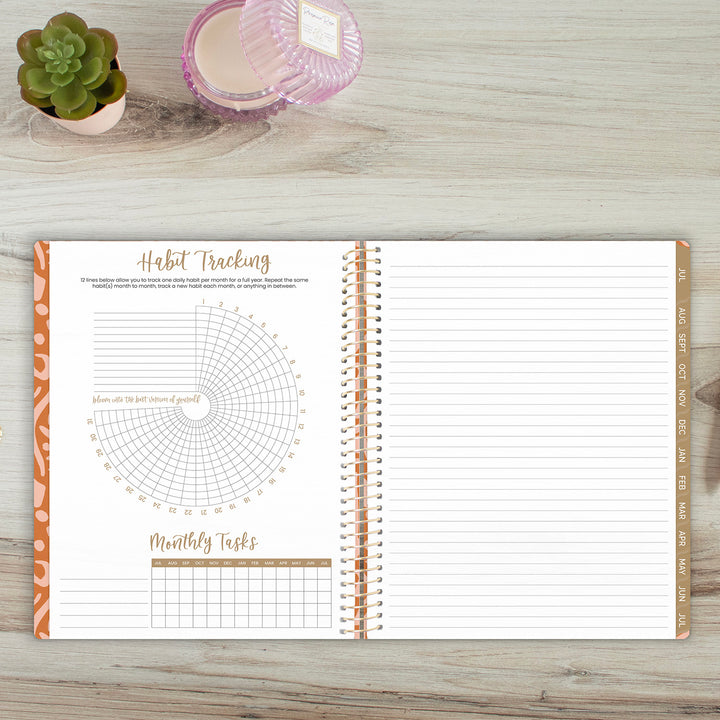 Open spiral-bound planner with habit tracking and monthly tasks sections on a wooden surface.