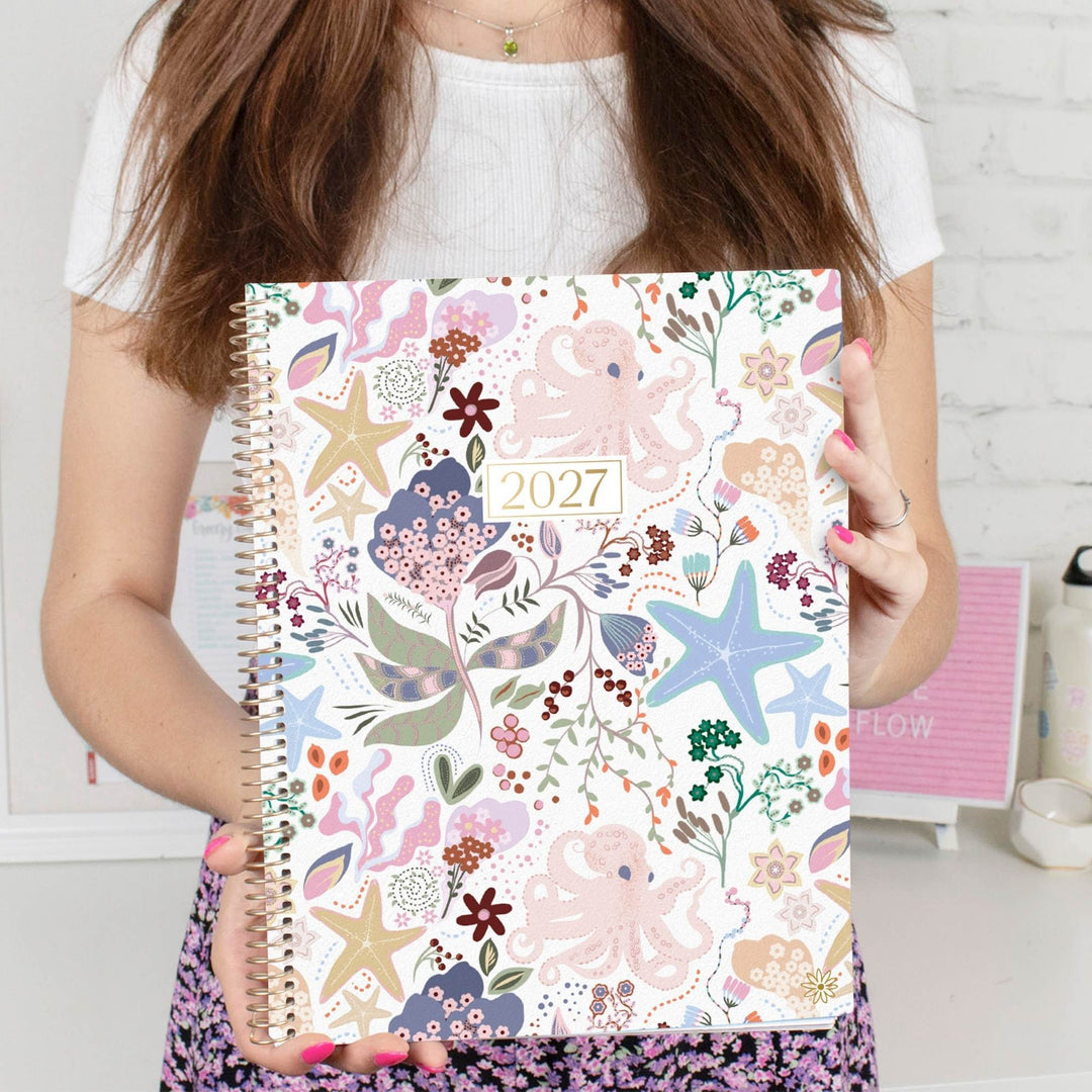 Person holding 2027 planner with colorful seaside starfish and floral pattern cover