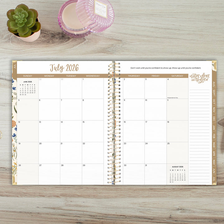 Open spiral-bound planner showing July 2026 on a wooden surface with a plant and candle.
