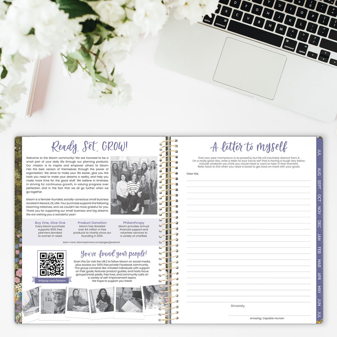Open planner with text and images on a desk with a laptop and flowers.
