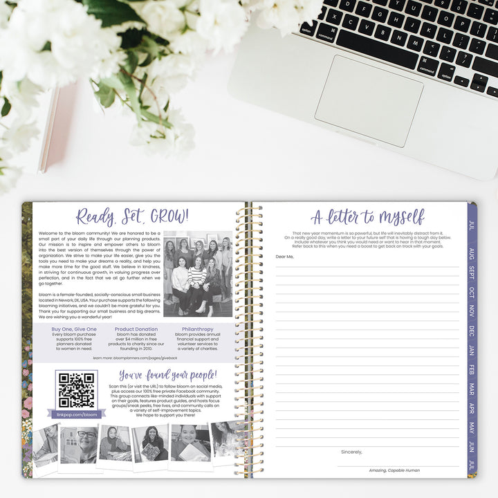 Open planner with text and images on a desk with a laptop and flowers.