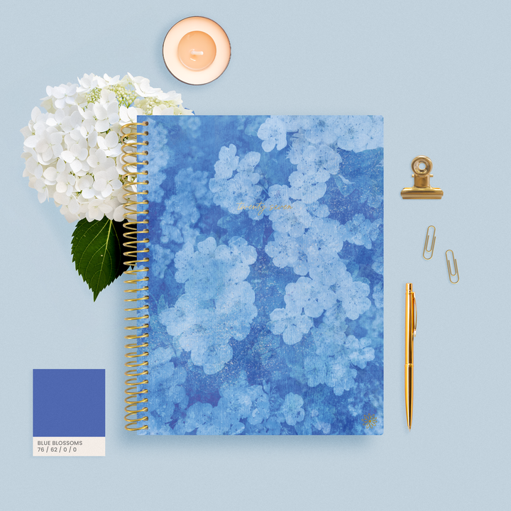 Blue Hydrangea 2027 Planner on a blue background with a flower, candle, pen and paperclips. 