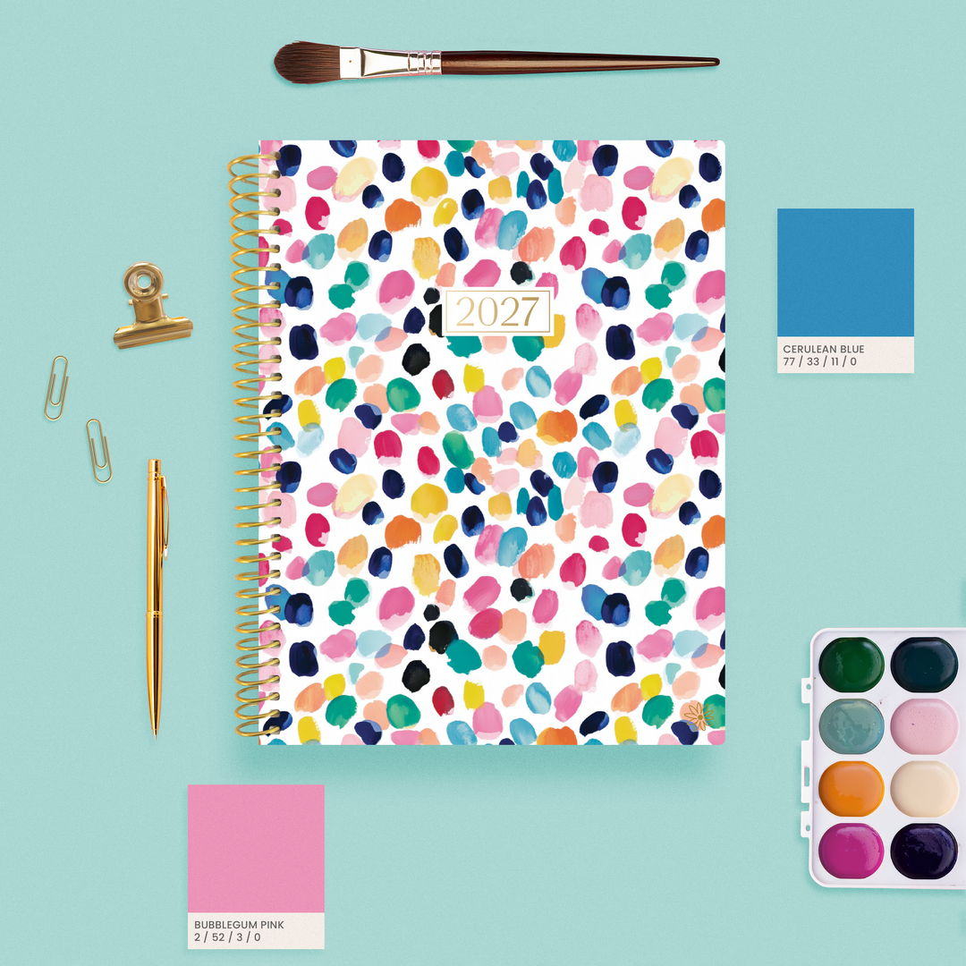 2027 Confetti bloom planner on a teal background surrounded by pain, brushes and pantone swatches.