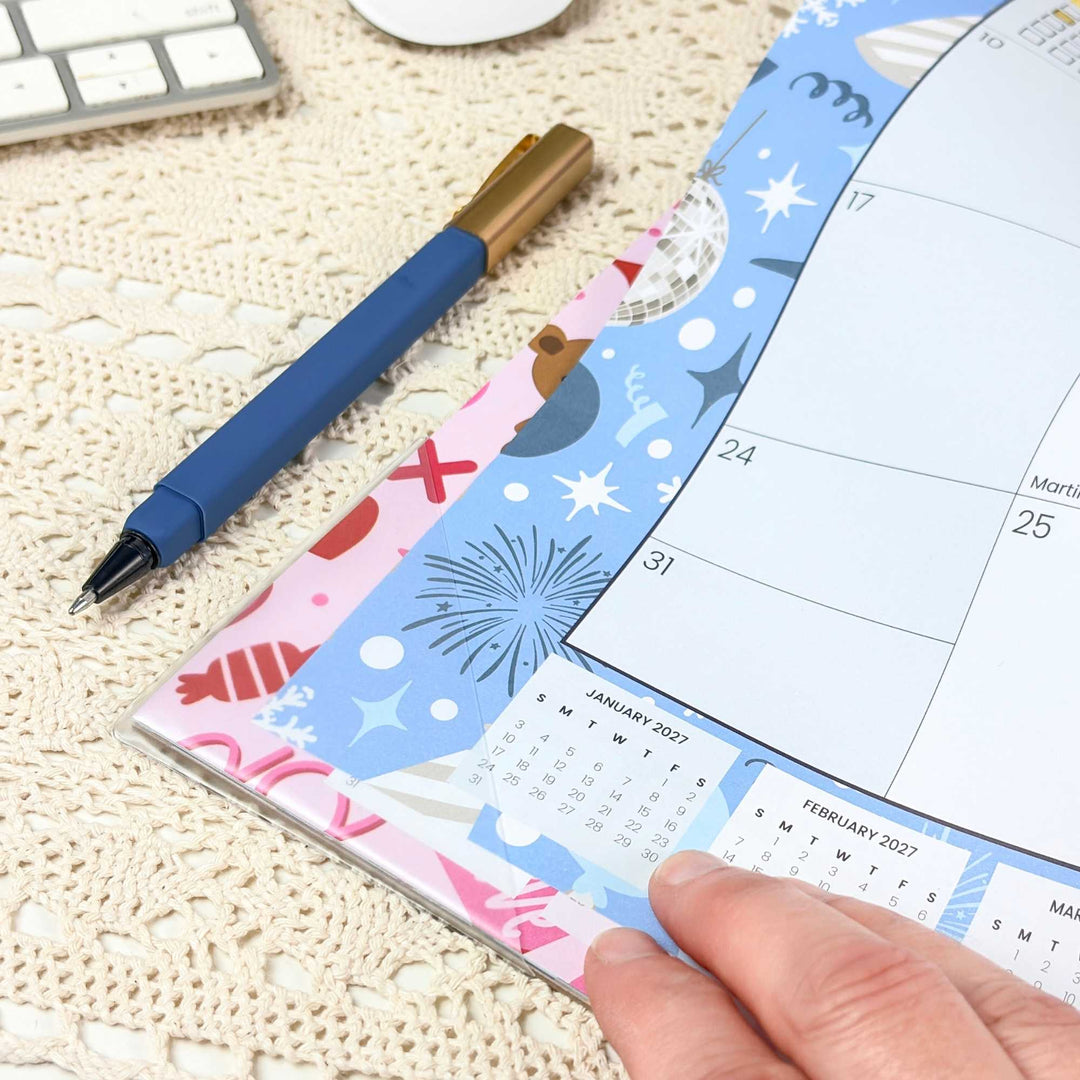 Small calendar with decorative cover on a textured surface, held by a hand.