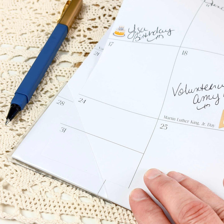Calendar with handwritten notes on a textured surface with two pens.