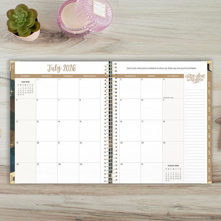 Calendar open to July 2026 on a wooden surface with decorative items.