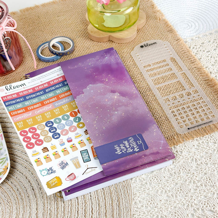 A planner sticker set and matching planner accessories arranged on a woven beige mat. The main product is a purple glittery planner cover with a matching sticker sheet featuring colorful labels and a clear plastic grid divider.