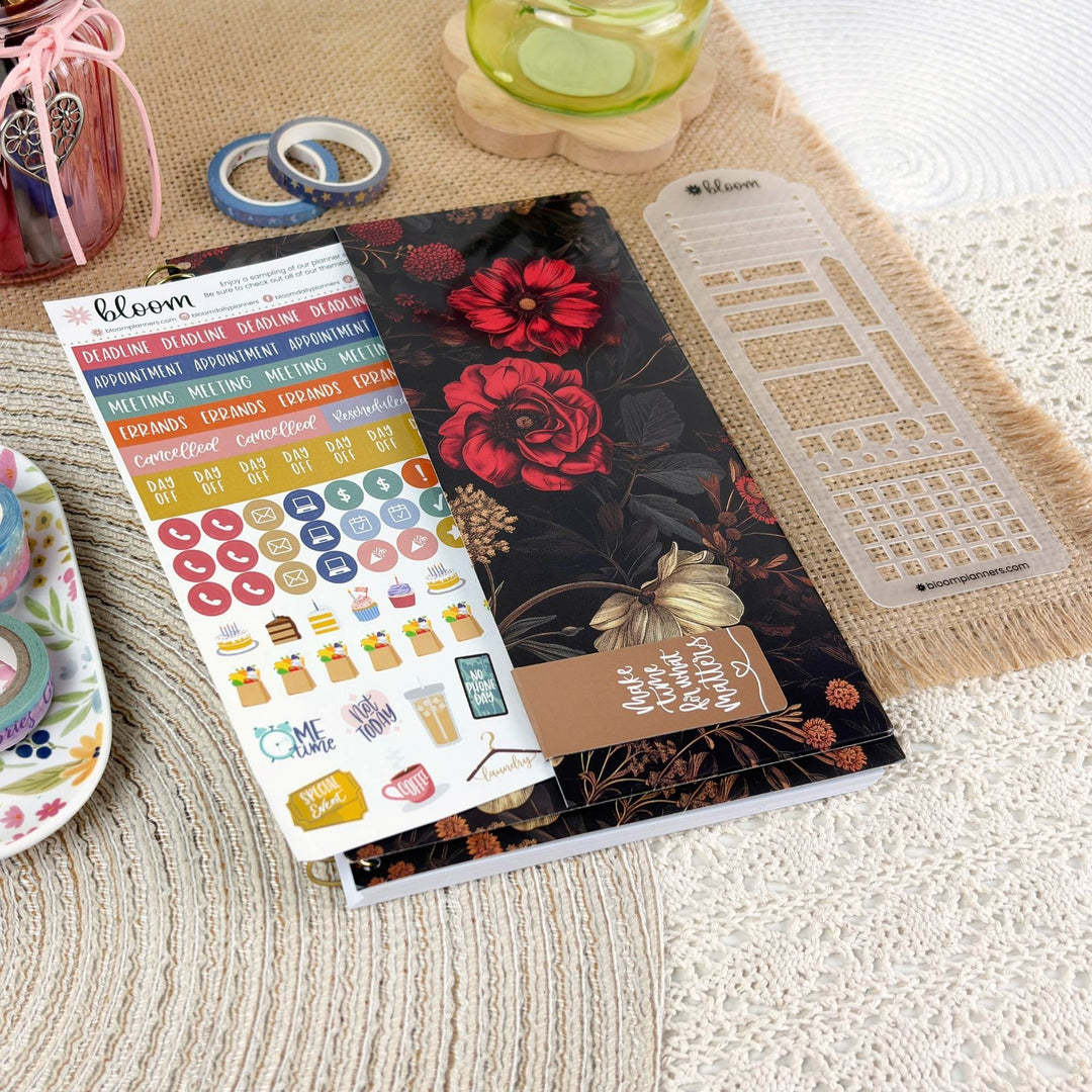 A planner sticker sheet and matching planner accessories arranged on a textured cream lace surface with a beige woven mat. The main product appears to be a Bloom planner sticker set, with floral planner cover art, colorful round and rectangular stickers, and a clear grid template visible.