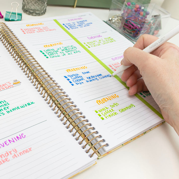 Person using a planner with colorful tasks on a desk.