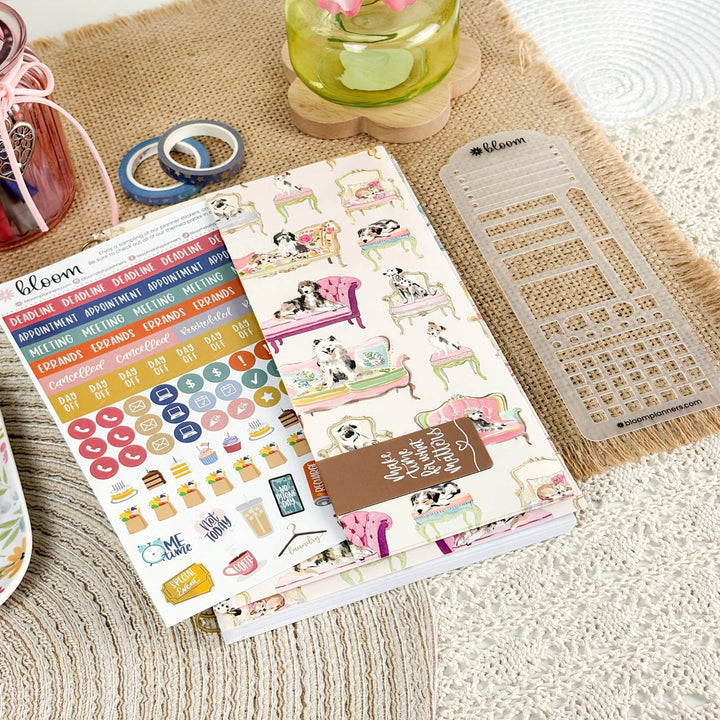 A planner sticker sheet set featuring dog-themed illustrations and colorful daily labels, styled on a beige woven mat with washi tape, a clear plastic divider, and a small jar in the background.