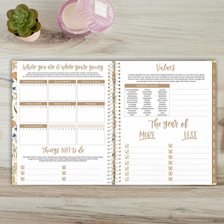Open planner on a wooden surface with a small plant and candle in the background