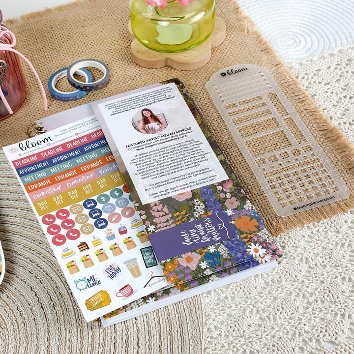A styled flat-lay of a Bloom planner sticker sheet set on a woven beige mat, featuring colorful category stickers, a floral-themed insert sheet, and a clear plastic grid template.
