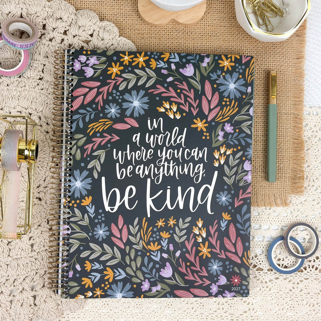 A spiral-bound notebook with a floral cover and the quote 'in a world where you can be anything. be kind.