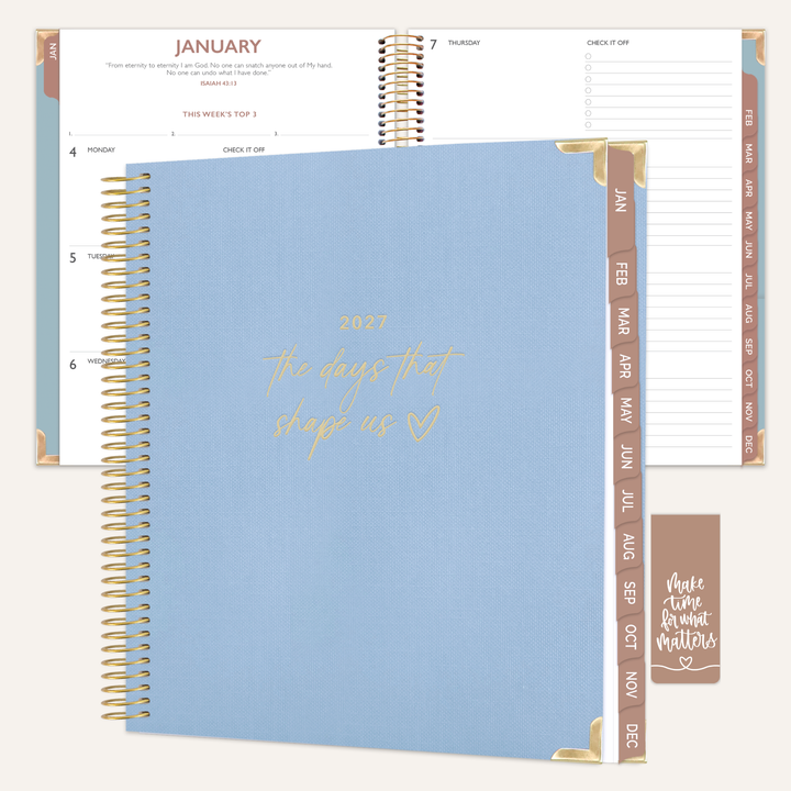 A spiral-bound planner shown open and closed on a light cream background. The closed cover is light blue with gold foil script reading '2027 the days that sleep us' and gold corner accents.