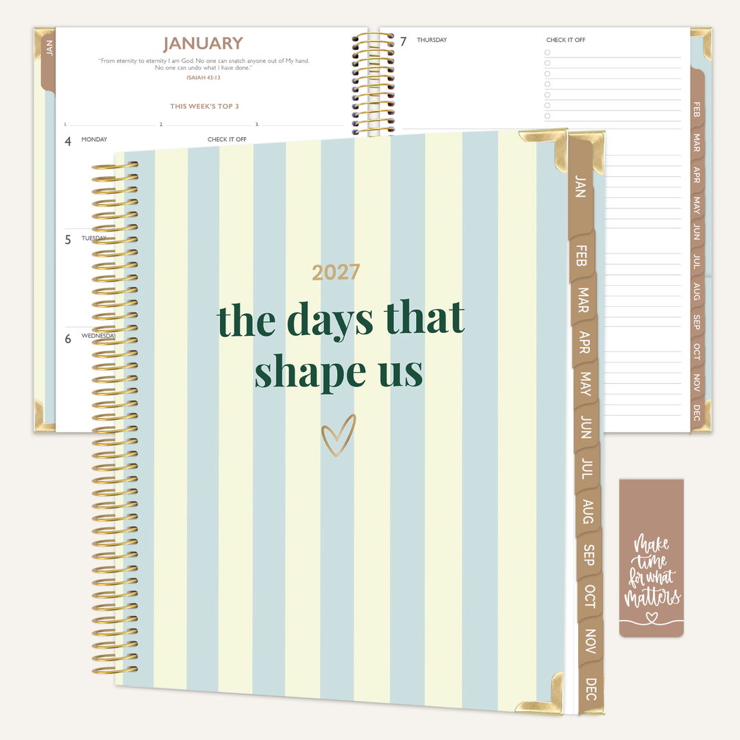 A spiral-bound planner shown open and closed, featuring pale blue and cream vertical stripes on the cover with the text '2027 the days that shape us' and gold-toned rings. Inside, the planner pages are white with gold and brown tabs and printed calendar details.