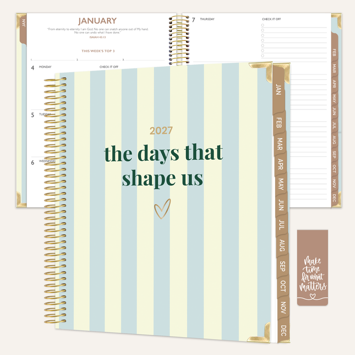 A spiral-bound planner shown open and closed, featuring pale blue and cream vertical stripes on the cover with the text '2027 the days that shape us' and gold-toned rings. Inside, the planner pages are white with gold and brown tabs and printed calendar details.