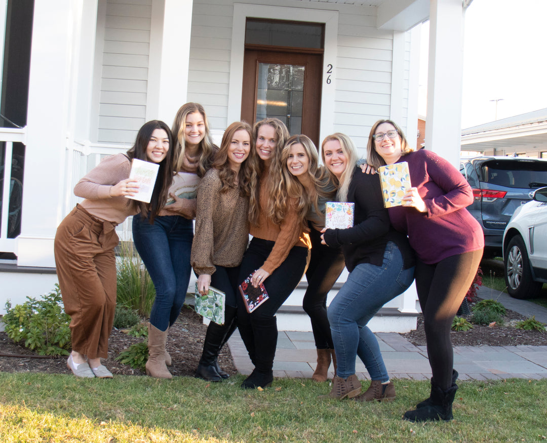 Group photo of the bloom team holding various bloom planners in front of a beach house