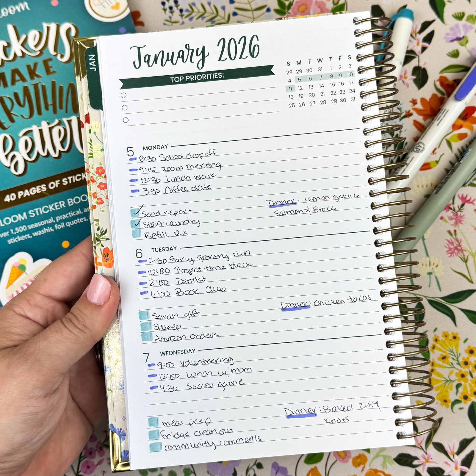 Hand holding a planner with January 2026 monthly schedule on a floral background