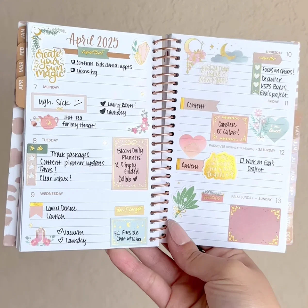 A hand displays a spiral-bound planner open to a decorated April 2025 week, featuring colorful stickers—including gold foil accents from the Planner Stickers, Simply Gilded x bloom Boho Celestial Sticker Pack by bloomdailyplanners—plus notes and reminders.